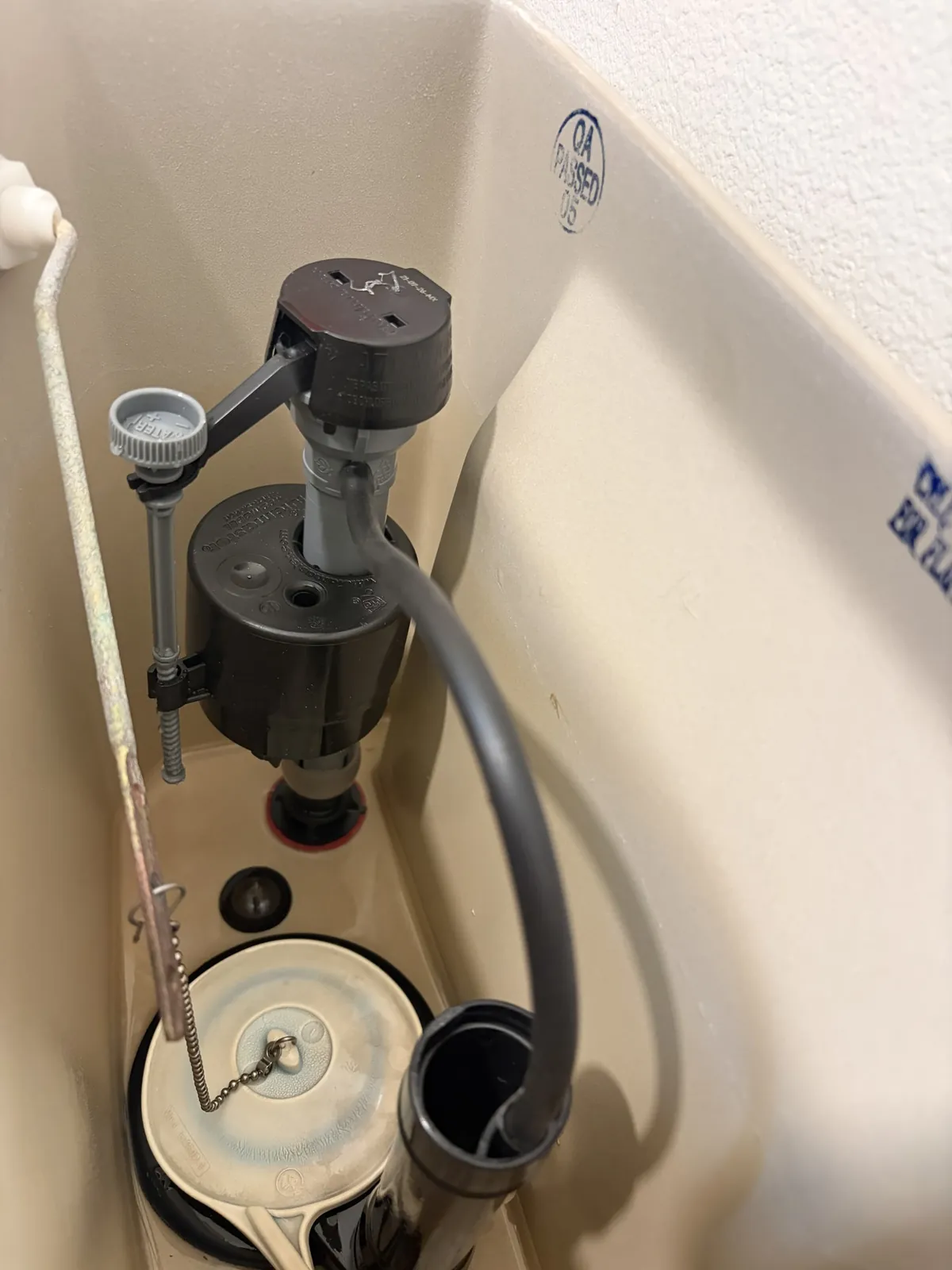 Inside a toilet tank showing the fill valve, supply hose and flapper