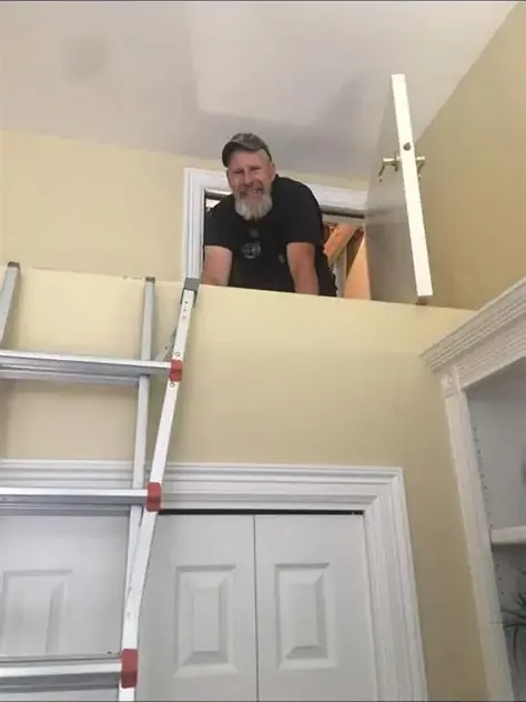 Plumber looking down from an attic access hatch above a ladder