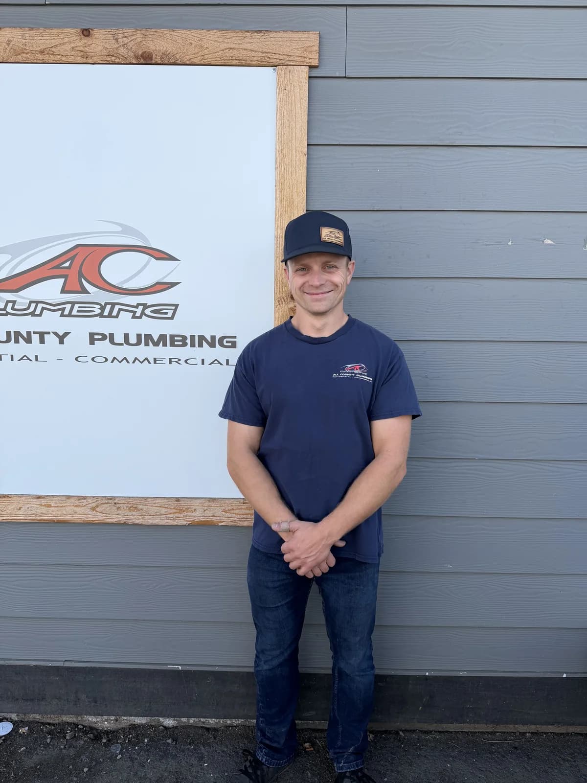 All County crew member beside the All County Plumbing shop sign